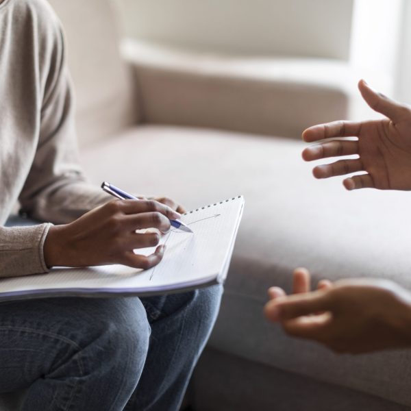 Cropped of black woman therapist holding folder and pen, african man gesturing while have professional aid psychological help, hands of unrecognizable doctor and patient, close up, copy space